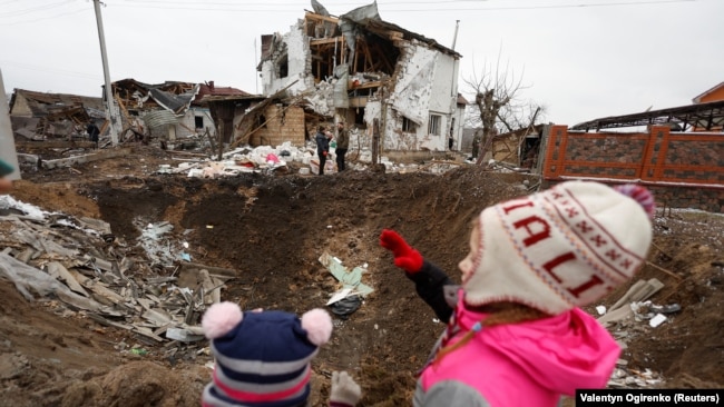 Діти дивляться на воронку, яка залишилася внаслідок російського ракетного удару у Глевасі на Київщині, 26 січня 2023 року