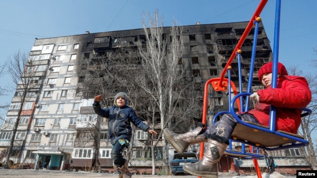 Діти в окупованому Маріуполі граються перед будівлею, яка була пошкоджена під час бойових дій в березні 2022 року