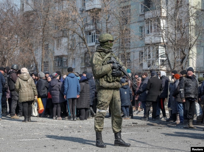 Солдат російської армії стоїть біля місцевих жителів в Маріуполі, березень 2022 рік