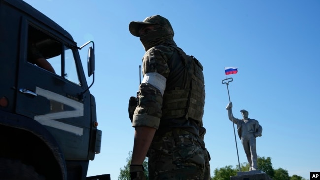 Військова вантажівка з літерою Z, яка стала символом російської армії, проїжджає повз російського солдата, який стоїть на дорозі на в’їзді до Маріуполя, червень 2022 року
